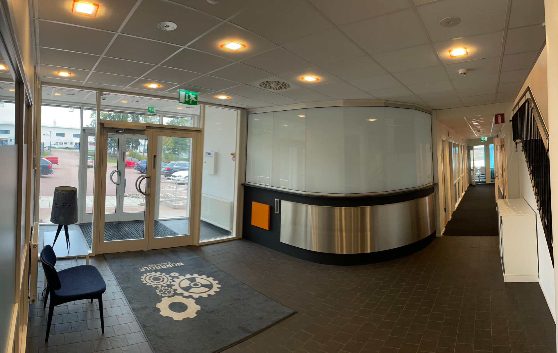 Entréhall med glasentré, rund receptiondisk i borstad metall och frostat glas samt matta med Norrböle Business Park-logotyp