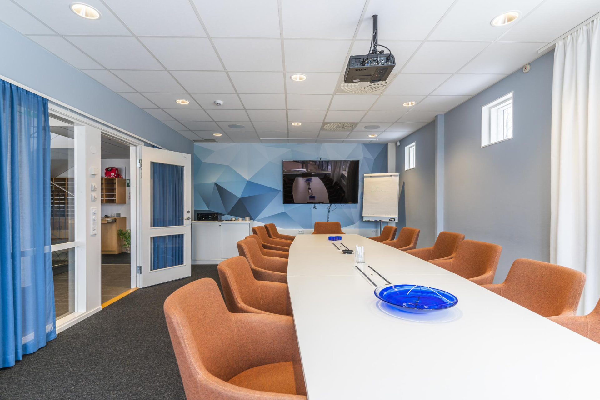 Konferensrum med långt mötesbord, projektor och skärm